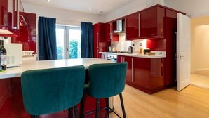 A modern kitchen with red cabinets, a white countertop, and two green bar stools.