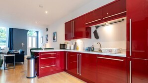 A modern kitchen with red cabinetry, a stainless steel trash bin, and a dining area with a table and chairs.