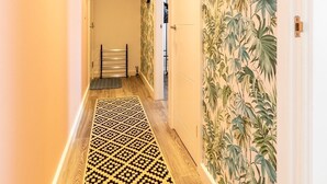 A hallway with a patterned rug, a phone on the wall, and a door with a plant-themed wallpaper.