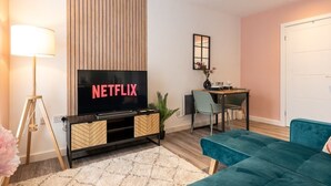 A modern living room with a flat-screen TV, a teal sofa, a dining table, and a lamp.