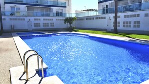 A swimming pool with a metal ladder, surrounded by a building with balconies and windows.