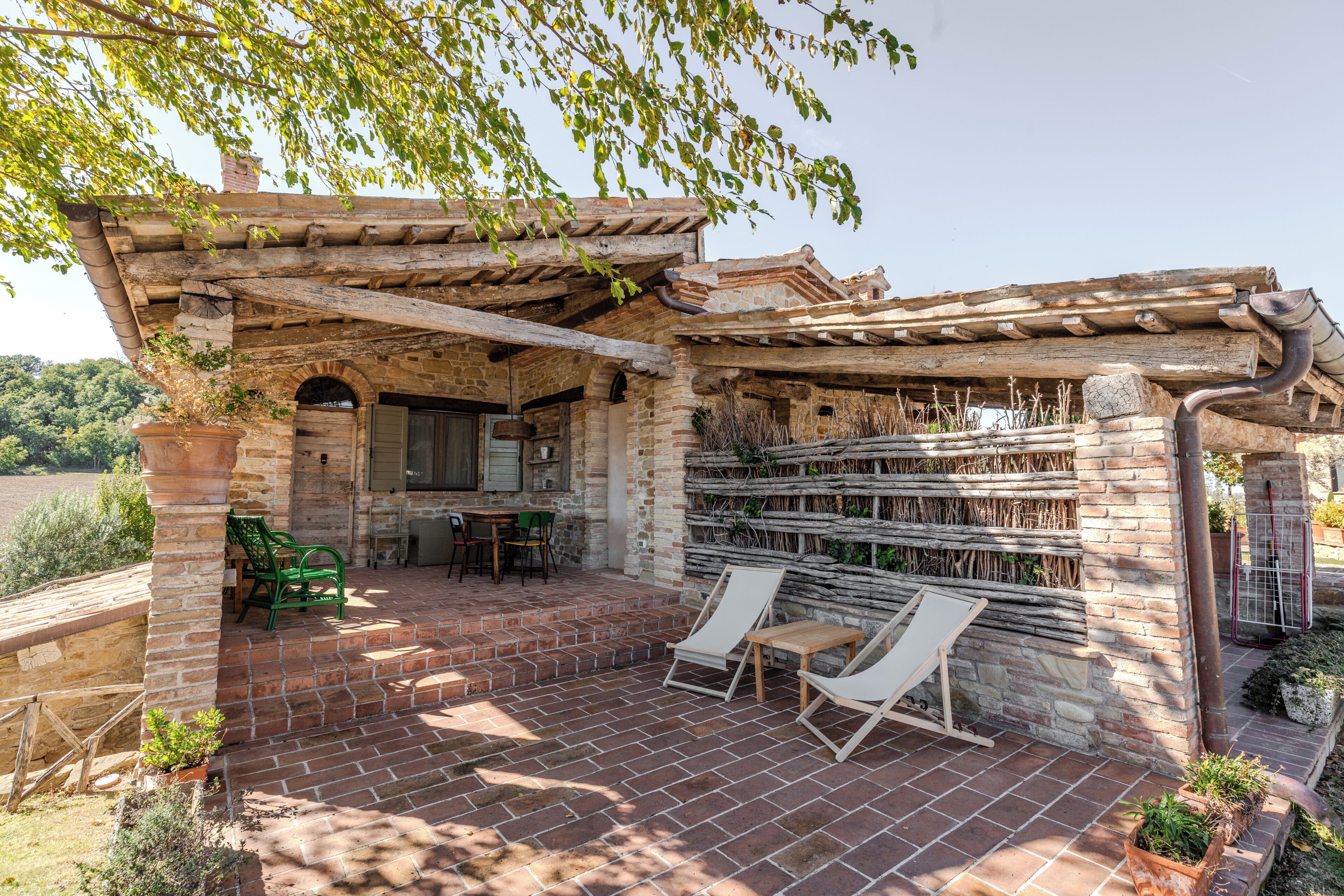 A patio with brick flooring, a pergola, and two lounge chairs.