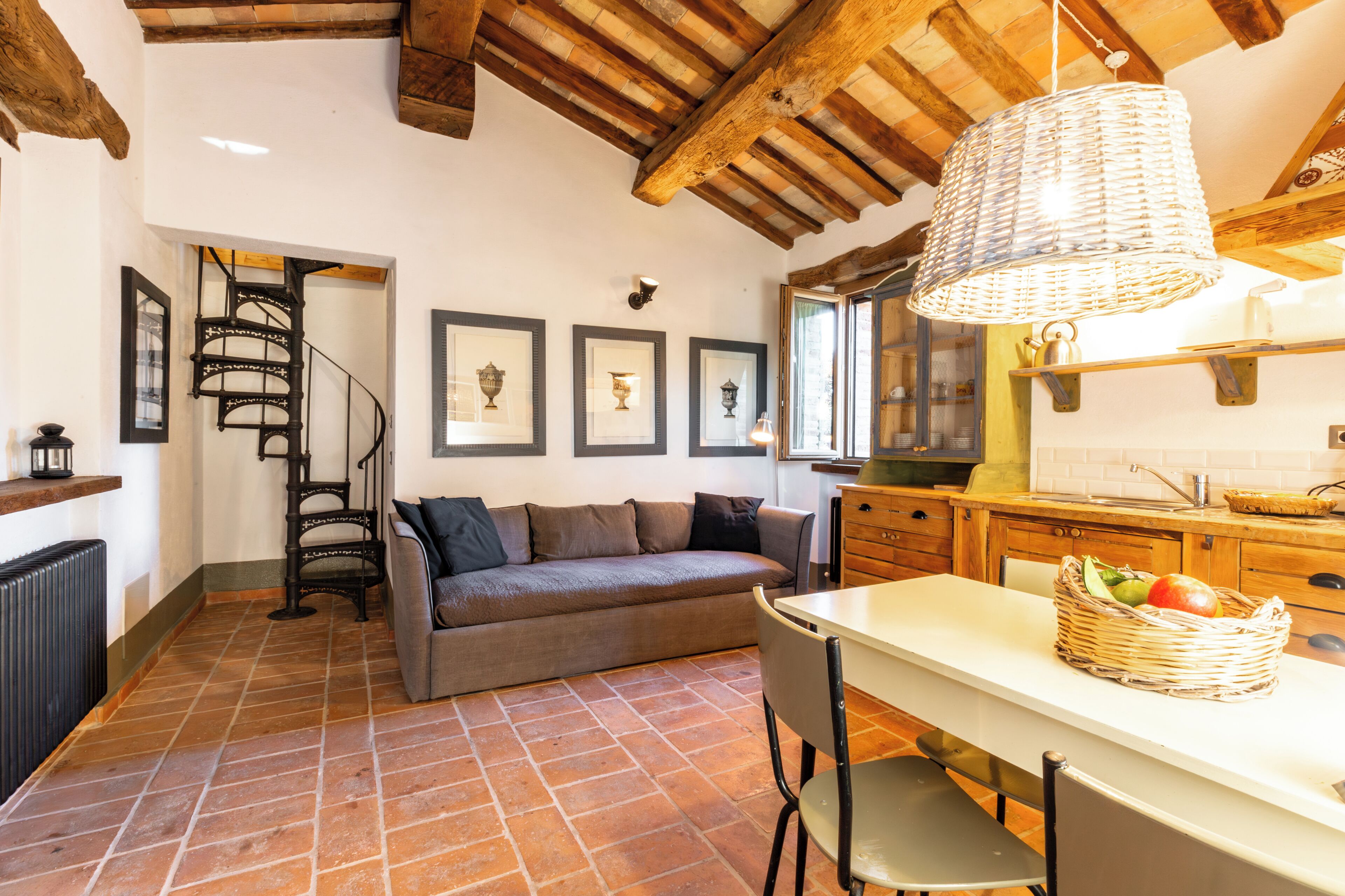 Un intérieur rustique avec des poutres apparentes, un escalier en colimaçon, un canapé, une table à manger et un coin cuisine.