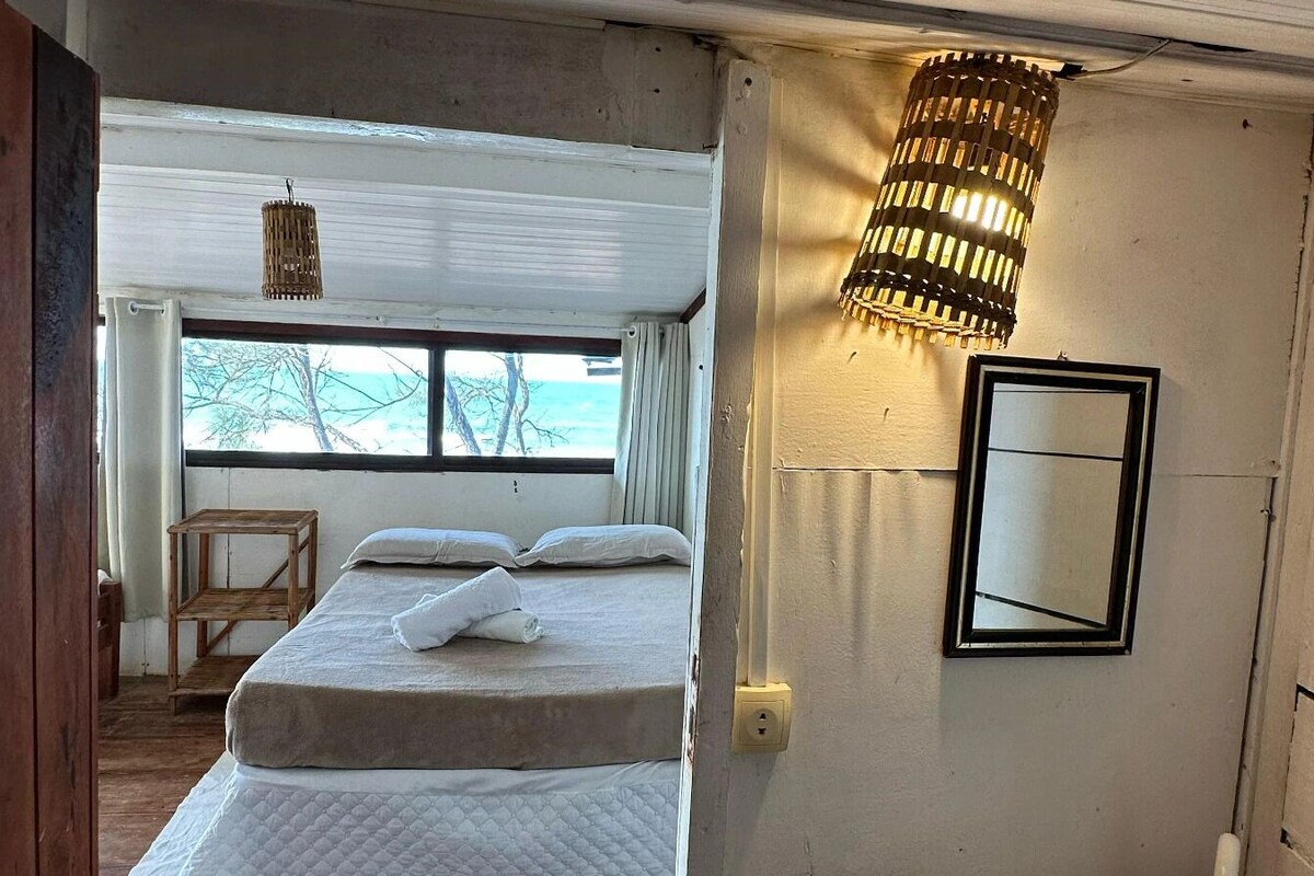 Une chambre à coucher comprenant un lit, une table de chevet, un luminaire suspendu, une fenêtre avec des rideaux et un miroir au mur.