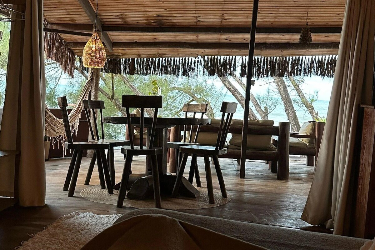 Un espace de vie à aire ouverte avec un plafond en bois, un luminaire suspendu et une vue sur l’océan.