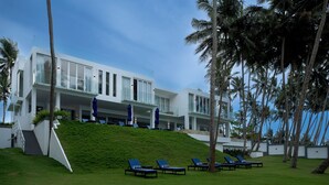 Un hotel moderno con fachada blanca, techo inclinado y zona de piscina con sillones de descanso.