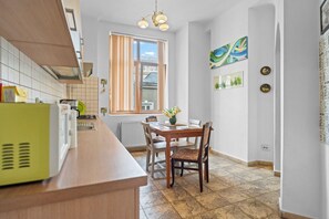 Una cucina con tavolo e sedie, una finestra con tende e un termosifone.