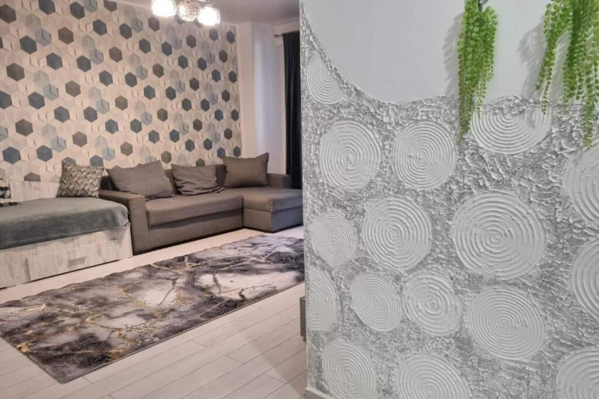 Een moderne woonkamer met een behang, een grijze bank en een decoratief vloerkleed.