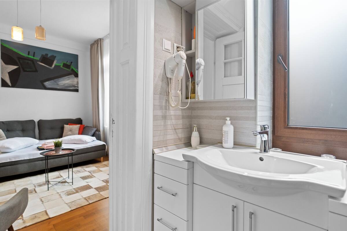 Een moderne badkamer met een grote wastafel, een spiegel en een aan de muur bevestigde haardroger.