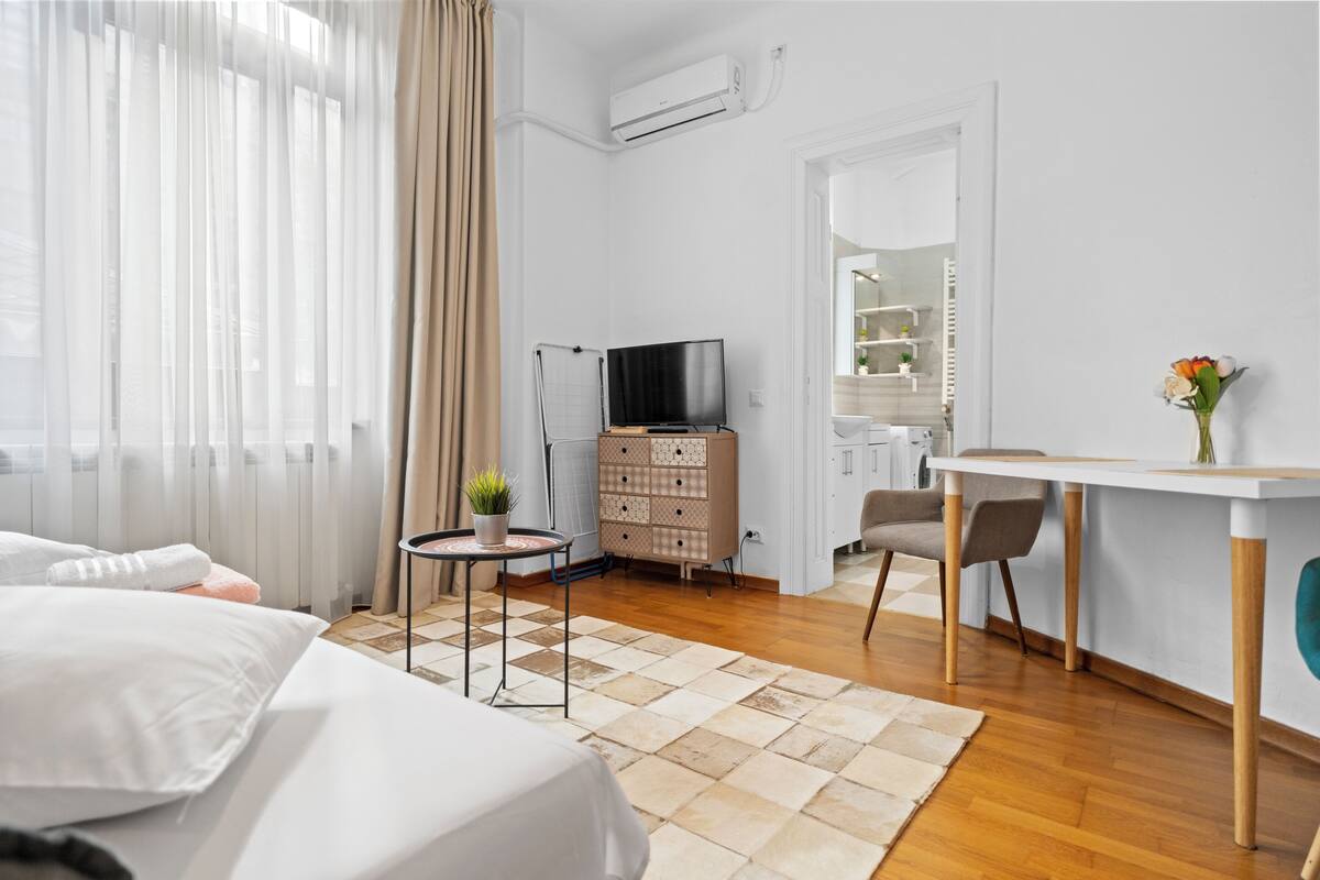 Hotelkamer met een bed, bureau, televisie, dressoir en een badkamer zichtbaar door een geopende deur.