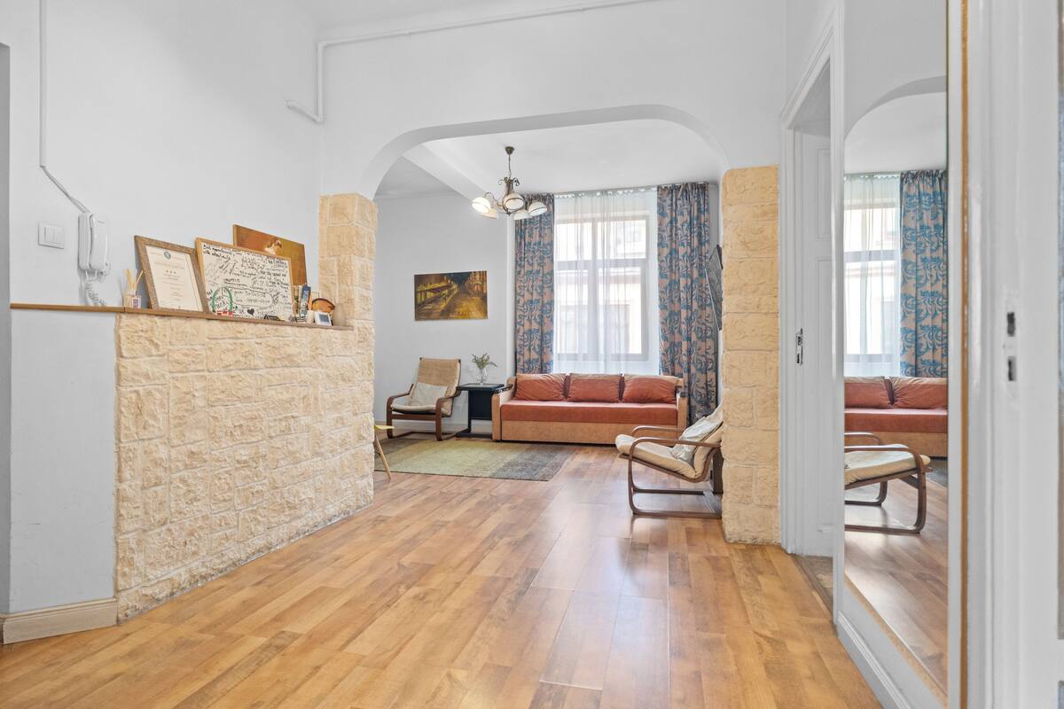 Een ruime woonkamer met houten vloeren, een accentmuur van steen, een bank, een fauteuil en een kleine tafel.