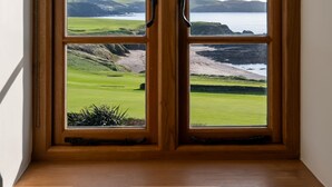 A window with a view of a coastal landscape, including grassy areas and a body of water. - Amber Tide -  a house that sleeps 8 guests  in 4 bedrooms (Thurlestone)