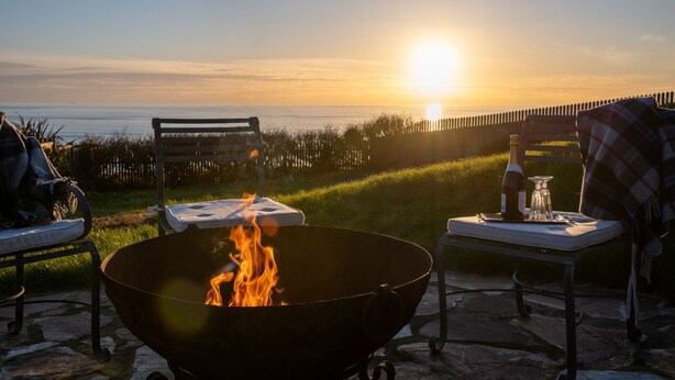A sunset view with a fire pit, outdoor seating, and a table with drinks. - Amber Tide -  a house that sleeps 8 guests  in 4 bedrooms (Thurlestone)