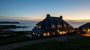 A large house with multiple rooms, a well-maintained lawn, and a view of the sea at dusk. - Amber Tide -  a house that sleeps 8 guests  in 4 bedrooms (Thurlestone)