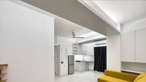 A modern living room with a yellow sofa, a kitchen area with white cabinets, and a ceiling fan. - 600sqft,5 Elite Stay with Pool, Sauna and Gym in Bashundhara (Dhaka)
