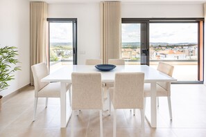 A dining area with a white table and chairs, a blue bowl, and a view of a residential area through large windows.