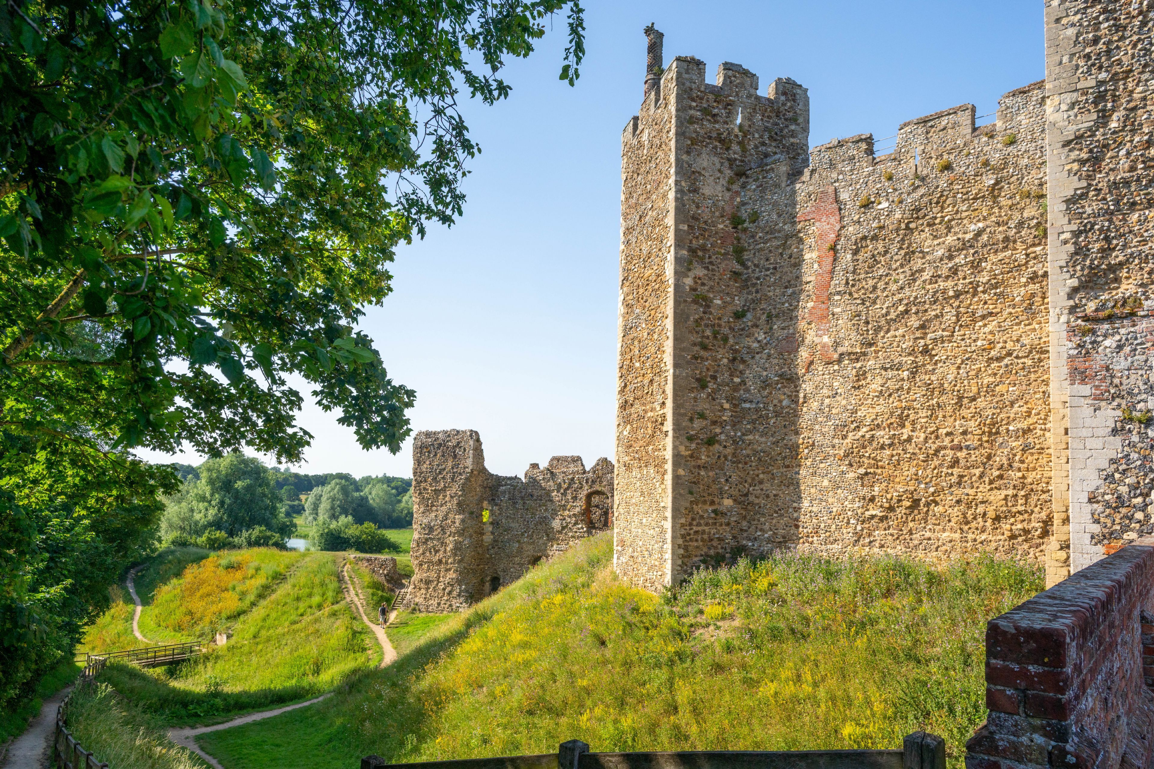 Un antico castello in pietra con una torre imponente, circondato da rigogliosa vegetazione e un sentiero sinuoso.