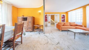 A living room with a dining area, a sofa, a coffee table, a cabinet, and a staircase leading to a second floor.