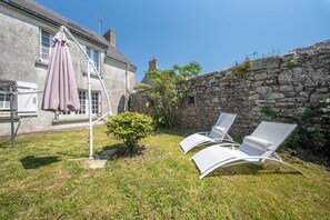 A stone wall, a small bush, and two white lounge chairs in a grassy area.