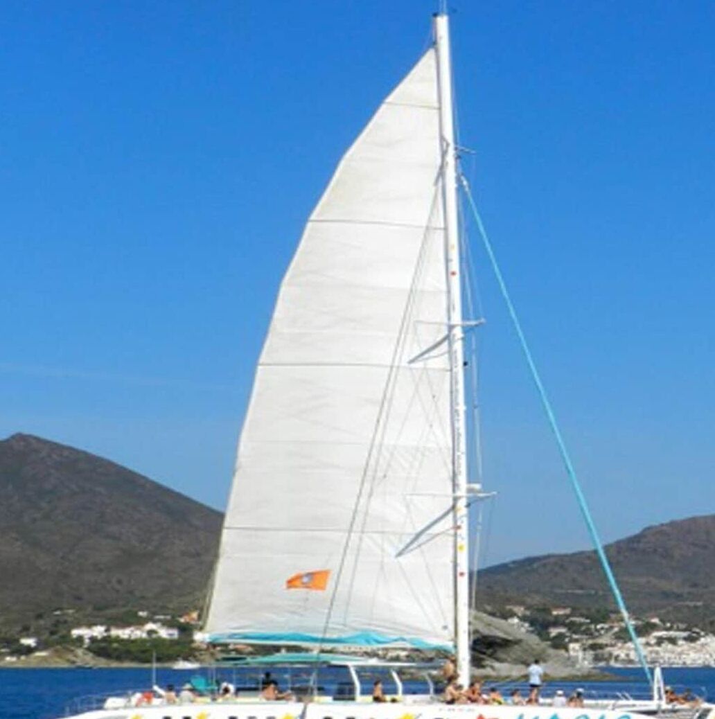 A sailboat with the word 'MAGIC' on its side, sailing on water with a mountainous backdrop.