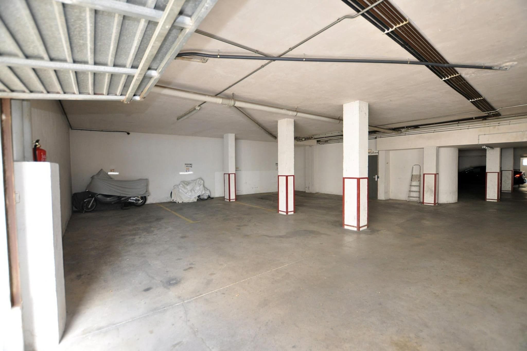 Un espacio interior amplio y vacío con pisos de concreto y pilares blancos, algunos con franjas rojas.