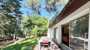 Un patio con mesa y sillas, un espacio de estar techado al aire libre, y vistas a zona boscosa.