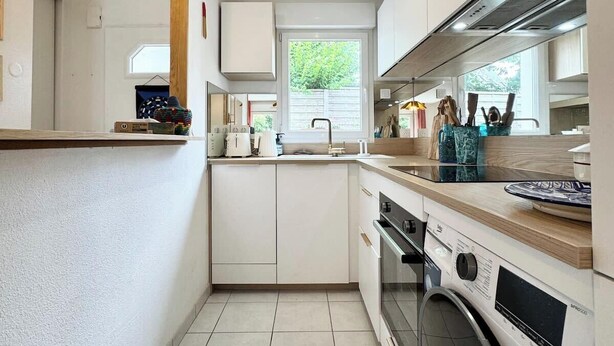 Una cocina moderna con armarios blancos, horno empotrado, lavadora y una ventana que proporciona luz natural.