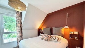 Un dormitorio con una cama grande, una lámpara colgante, una mesita de noche y una ventana con cortinas.