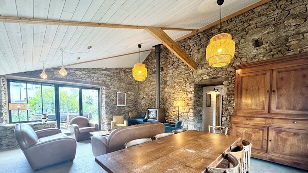 Un vaste espace dédié à la salle à manger, avec une grande table en bois et de nombreuses chaises, un mur en pierre et un buffet en bois rustique.