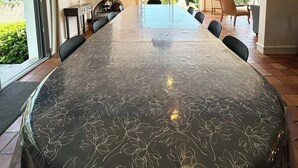 A spacious dining area with a long table, modern pendant lights, and large windows offering a view of the outdoors.