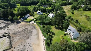 An aerial view of a coastal property with multiple houses, a beach, and surrounding greenery.