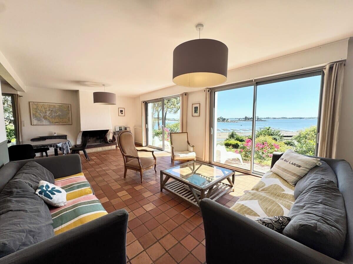 A spacious living room with a large window offering a view of the sea, a fireplace, and a dining area.