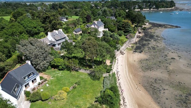 An aerial view of a coastal residential area with houses, a beach, and a body of water.