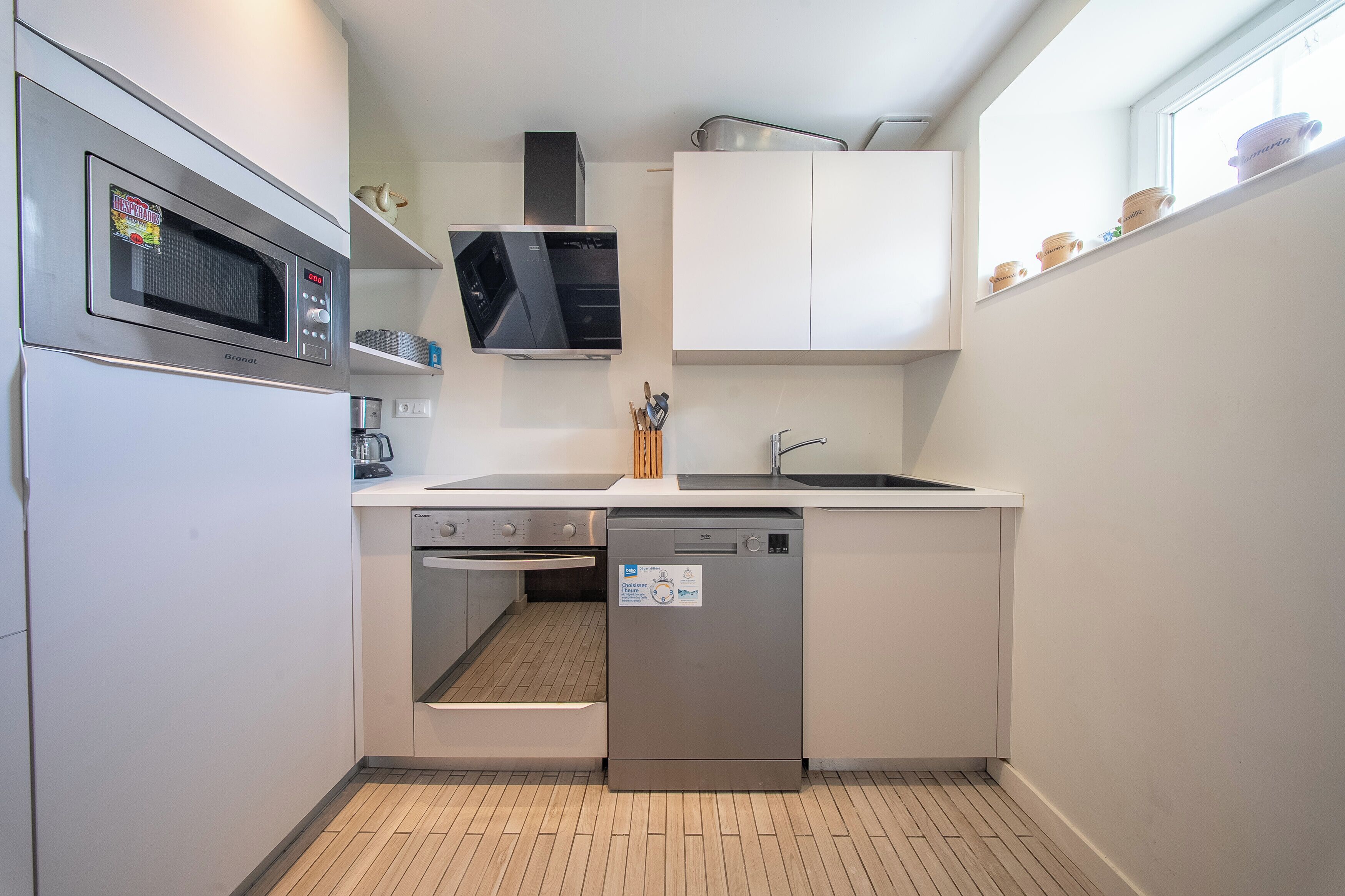 A compact kitchen with a microwave, oven, dishwasher, and a window above the sink.