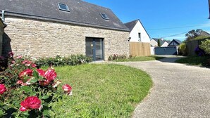 A stone house with a gravel driveway and a small garden with pink flowers.