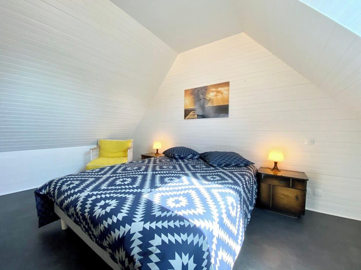 Une chambre à coucher avec un lit, deux tables de chevet avec des lampes, une chaise jaune et un tableau au mur.