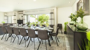 A modern dining area with a large table set for six, surrounded by chairs, and a kitchen in the background. - Comfort & fun w/ pool & games area (Armação de Pêra)