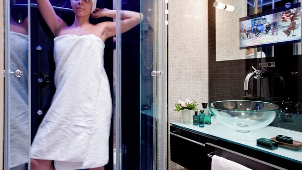 A modern bathroom with a glass-enclosed shower, a large glass bowl sink, and a flat-screen TV mounted above the sink. - De Luxe Inn 6 Guest House (Rome)