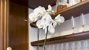 A bar area with a bottle of Cristal champagne in a glass bucket, surrounded by ice, and a potted orchid. Behind the bar, there are shelves with wine glasses and bottles. - De Luxe Inn 6 Guest House (Rome)