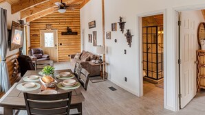 L’intérieur d’un chalet confortable en bois, avec un espace repas, un salon et une salle de bain visibles à travers une porte ouverte.