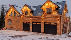 Une cabane en rondins avec un toit en métal, plusieurs portes de garage et un escalier menant à l’entrée.