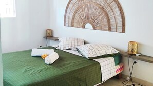 Une pièce avec un plafond en bois, un lit avec une literie verte, une décoration murale, une table de chevet avec une lampe et un tapis coloré.