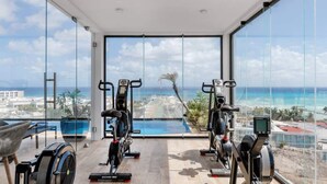 Ett modernt gym med träningsutrustning och ett stort fönster med utsikt över ett vackert hav och stadslandskap.