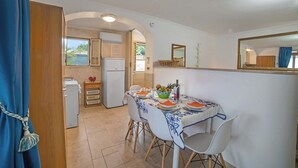 A dining area with a table set for two, a refrigerator, and a view of the outdoors through a window.