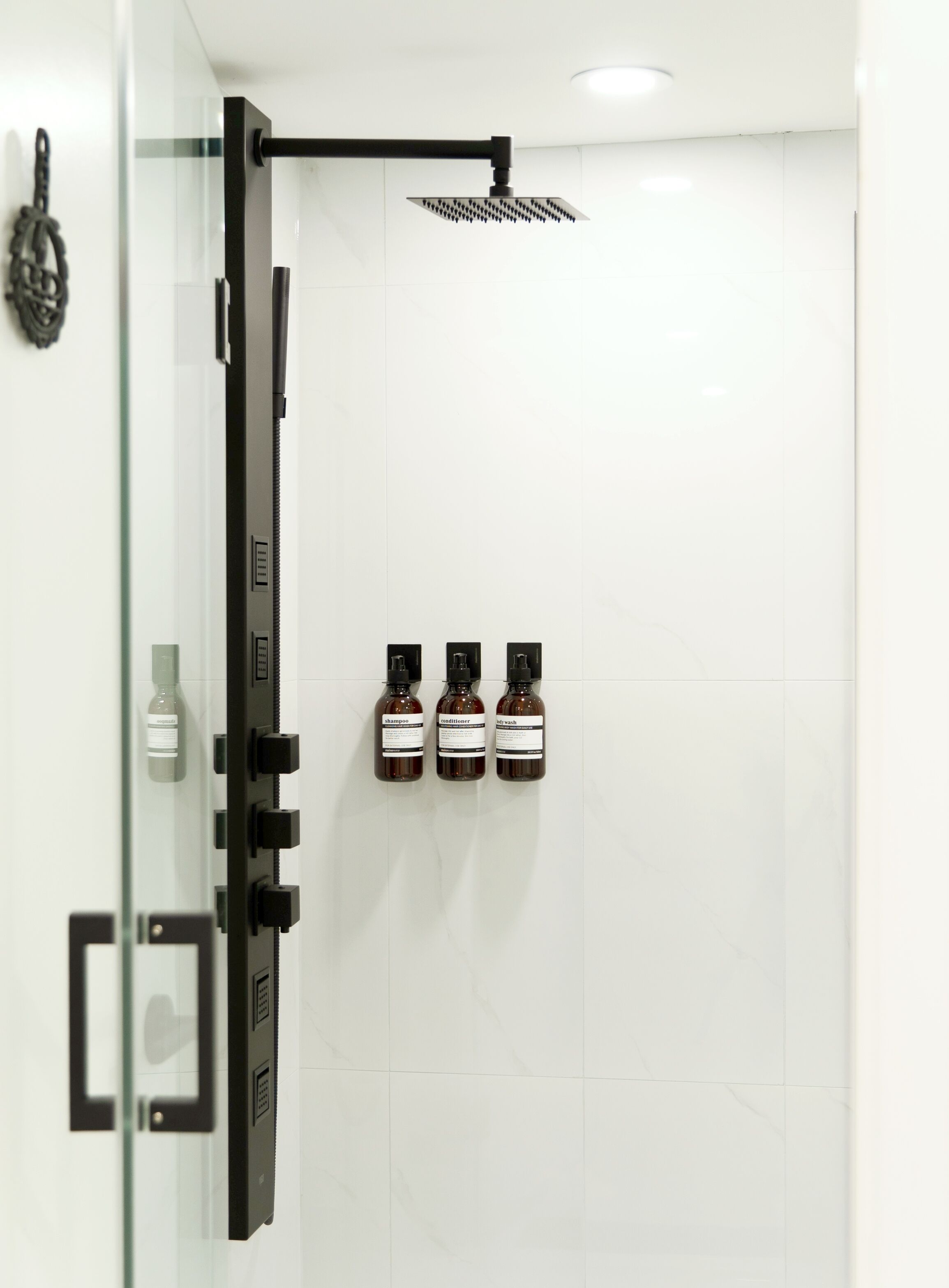 Une douche moderne dotée d’un pommeau de douche à effet pluie et de trois flacons de shampoing, d’après-shampoing et de gel douche.