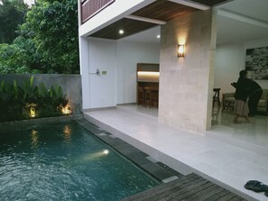 Ein moderner Poolbereich im Freien mit einer Holzterrasse, einer Sitzecke und einer Steinmauer.