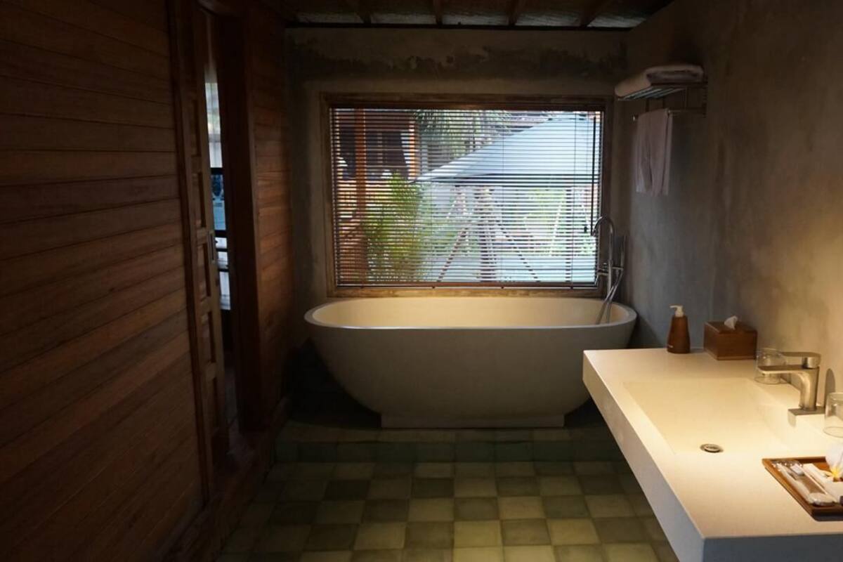 Une salle de bain avec une baignoire sur pieds, un lavabo blanc et une fenêtre avec des stores.