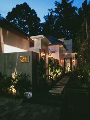 Une villa moderne avec un chemin de pierre menant à l’entrée, entourée d’une végétation luxuriante.