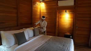 Een houten kamer met een bed, kussens, een nachtkastje en een kleine tafel met een fruitmand.