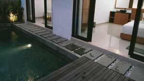 Een moderne slaapkamer met een groot bed, een nachtkastje en een spiegel. Er is een kleine badkamer met toilet en wastafel. De kamer heeft grote ramen en uitzicht op buiten.